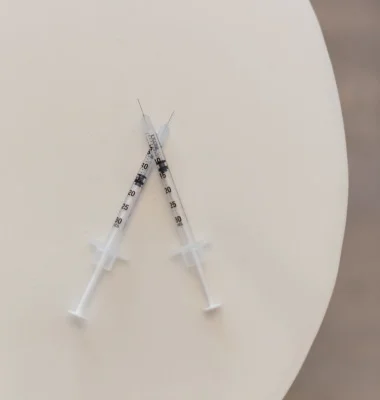 Two insulin syringes crossed on white surface in medical office setting