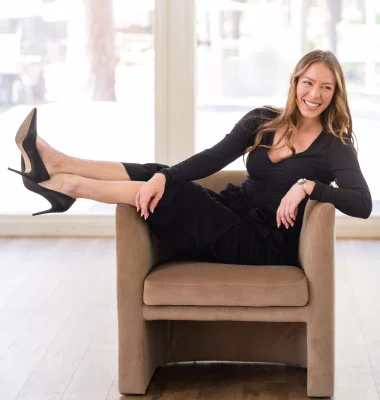Professional woman in black attire sitting confidently in modern office chair with bright windows in background