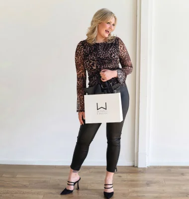 Woman in sequined top and black pants holding white handbag, wearing black heels in professional portrait