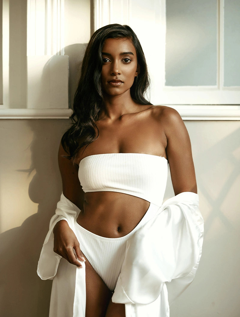 Woman in white bandeau top and matching bottoms posing in natural sunlight by window