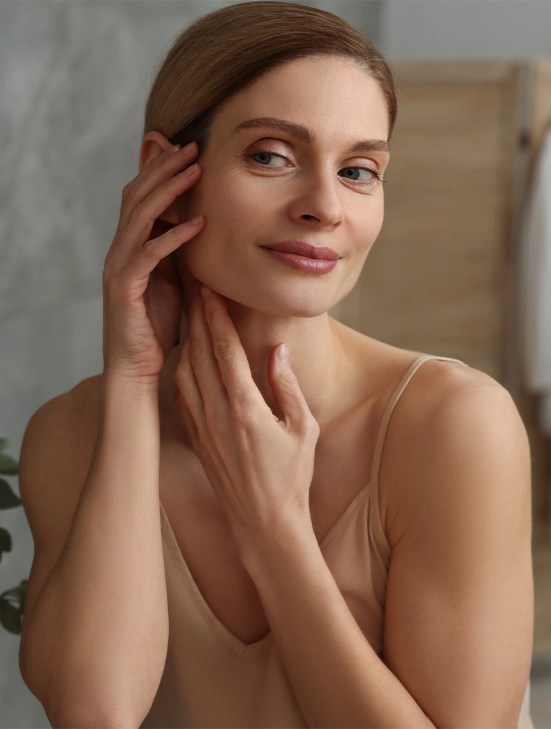 Woman with glowing skin touching face and neck demonstrating skincare routine and natural beauty