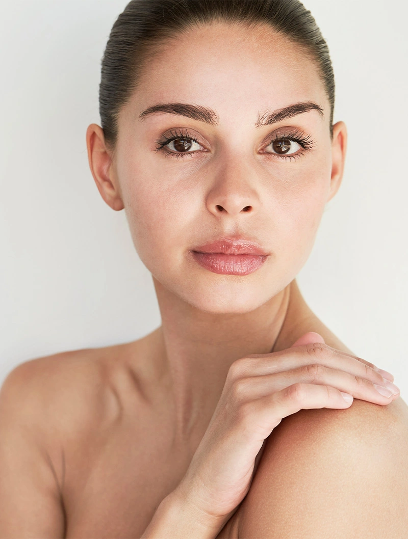 Natural beauty portrait of woman with clear glowing skin and minimal makeup touching shoulder