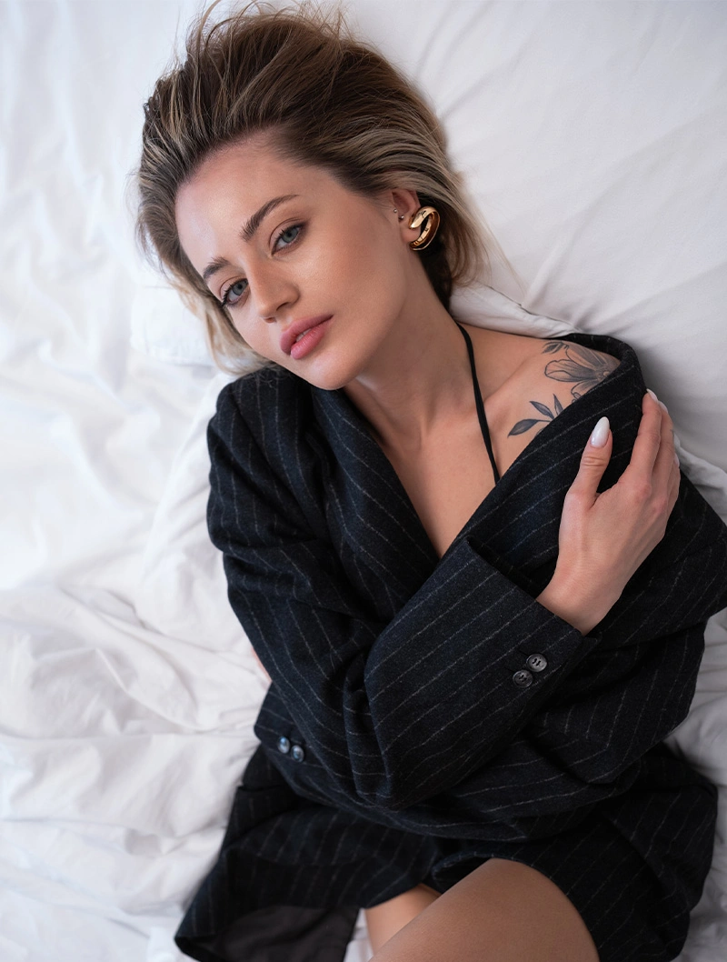 Woman in black robe relaxing on white bedding with natural makeup and elegant styling