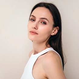 Professional woman with dark hair in white sleeveless top against neutral background, looking confidently at camera