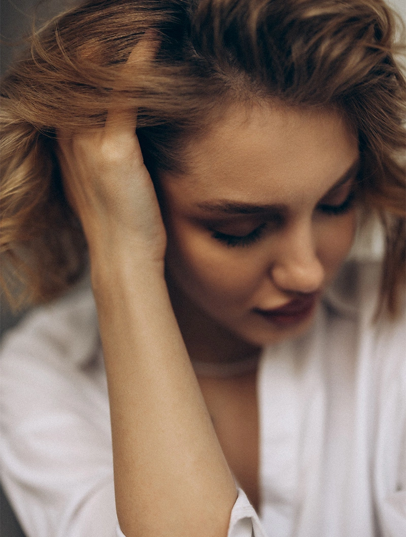 Woman with hand on head looking down appearing stressed or troubled in white shirt