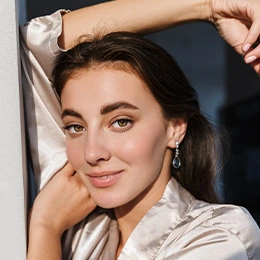 Woman with dark hair in white satin shirt posing with arms raised against dark background