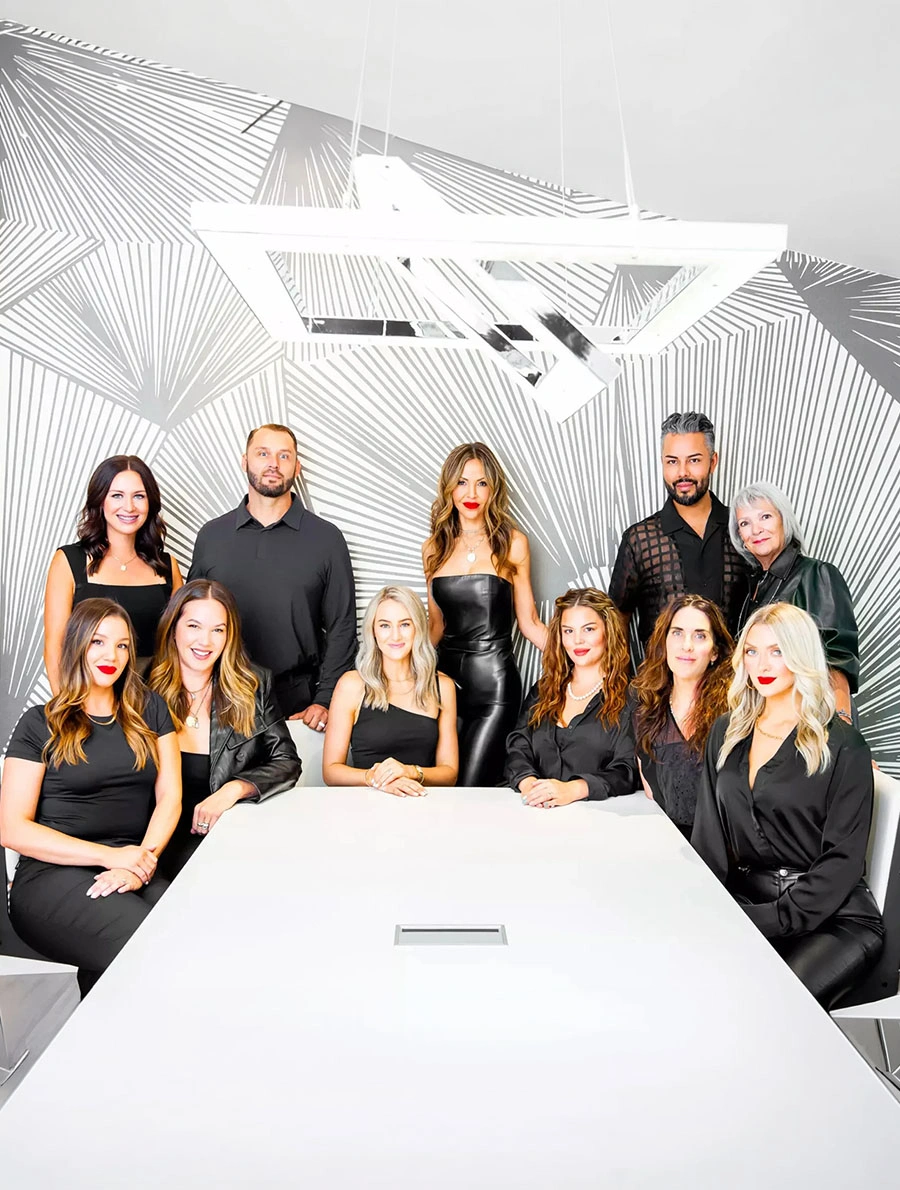 Professional real estate team of nine agents in black attire gathered around white conference table