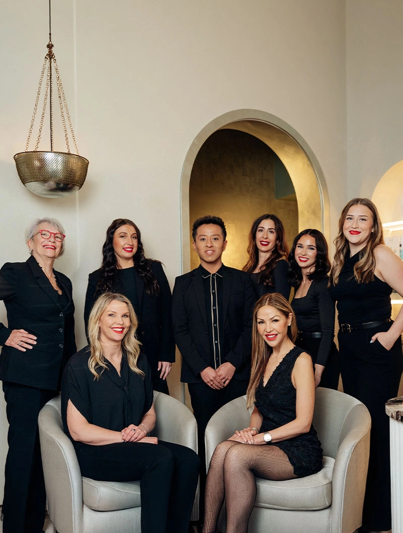 Professional team of seven women in black attire posing in modern office space with archway - in Bend, OR